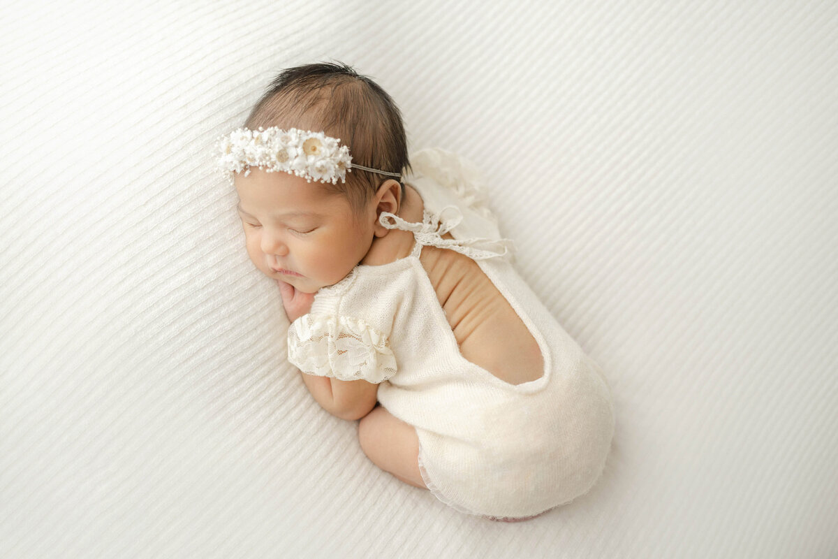 newborn baby girl sleeping with an adorable neutral outfit as you can see her baby rolls in a natural light oklahoma studio