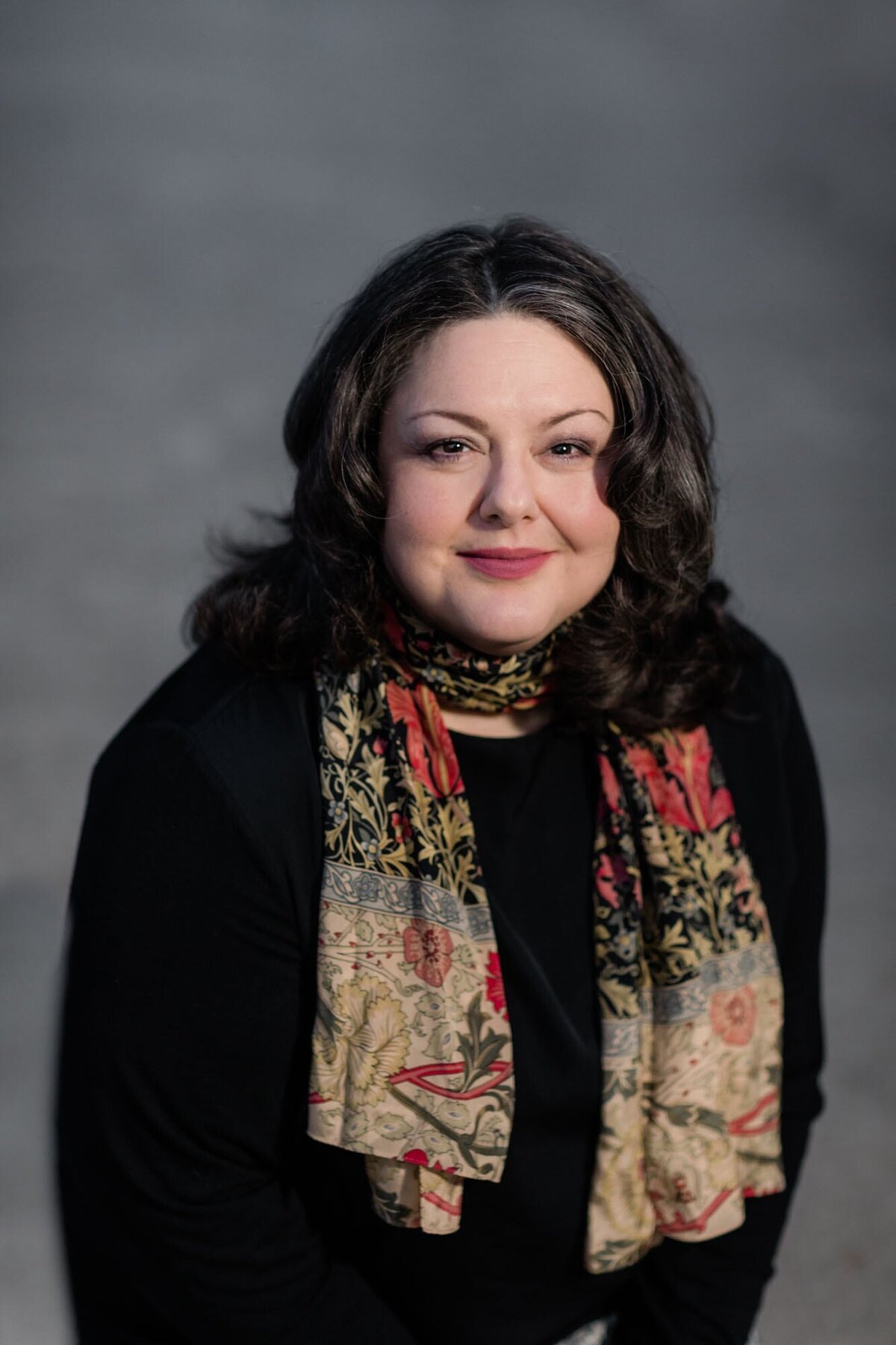 Dramatic headshot of a woma wearing a black shirt and a floral scarf.