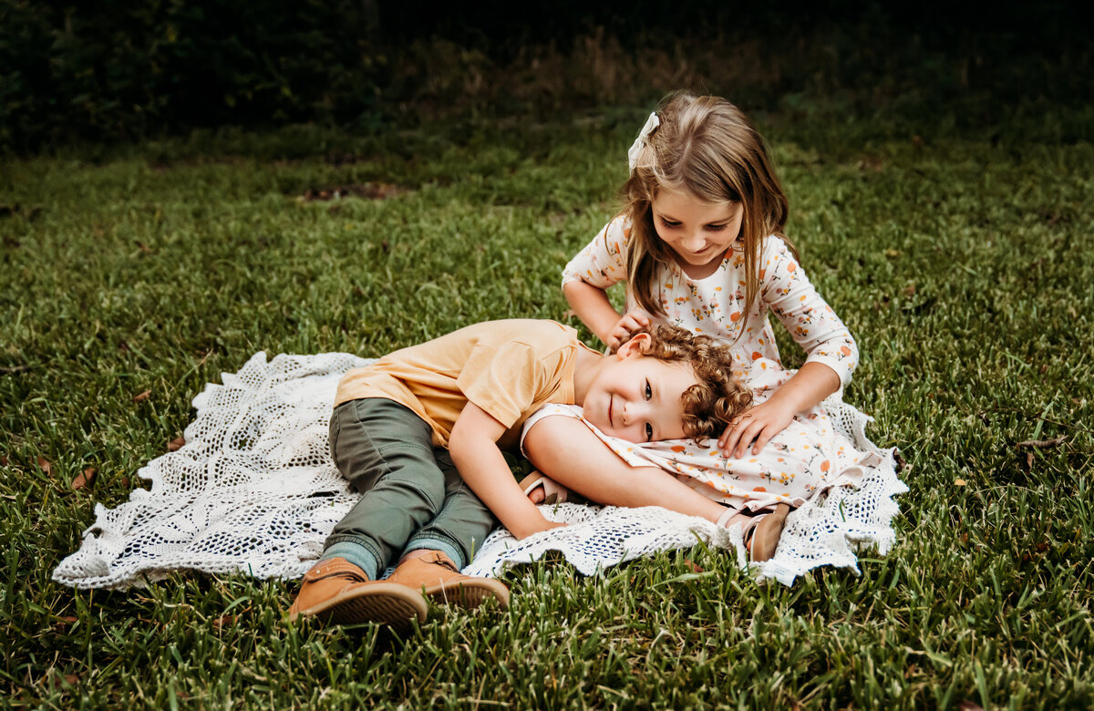 Family Photographer, a little boy lays on his sister's lap in the grass