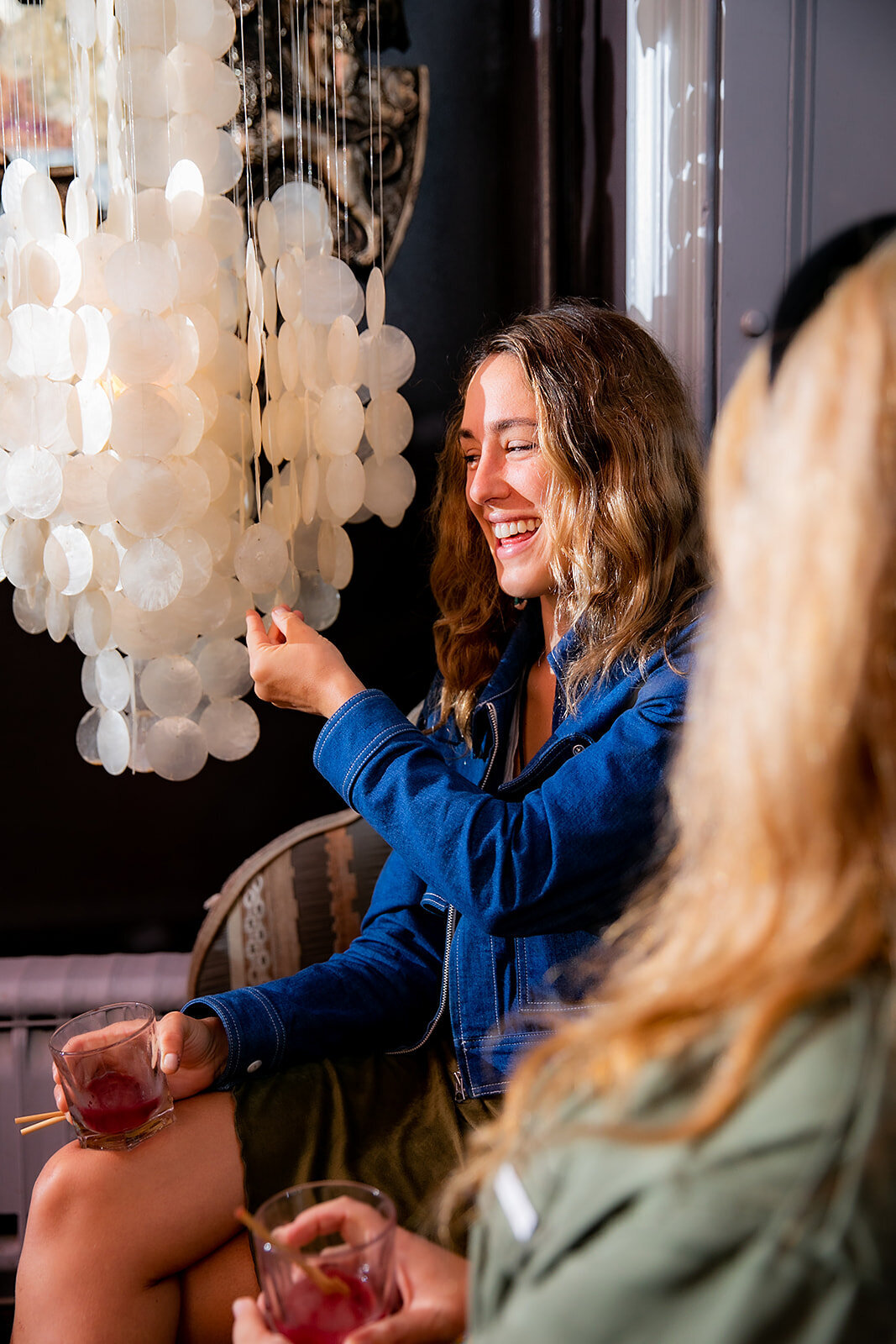 Guest enjoys a drink and smiles while interacting with a shell chandelier.
