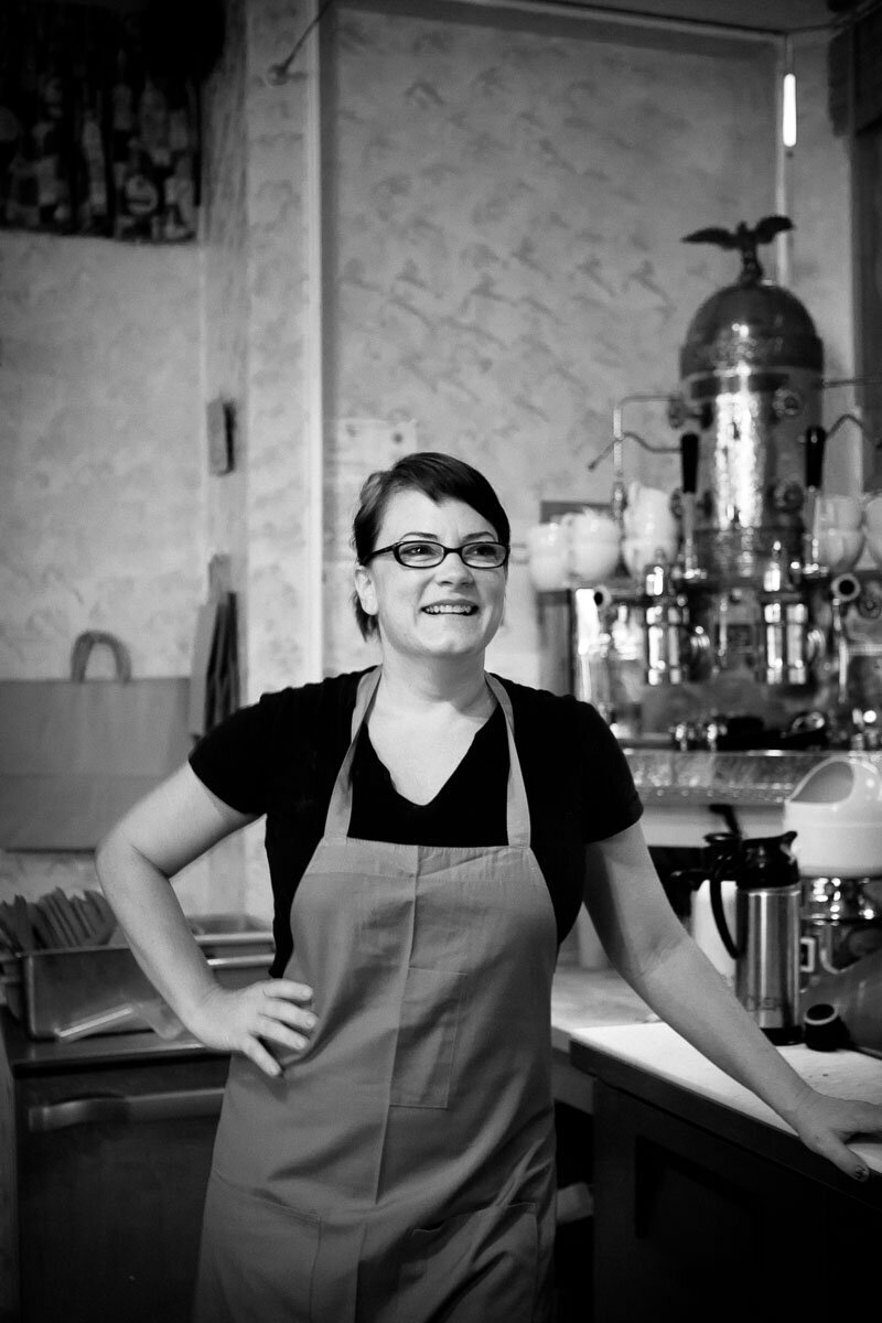 black and white photo of a coffee barista standing in front of an antique copper espresso machine