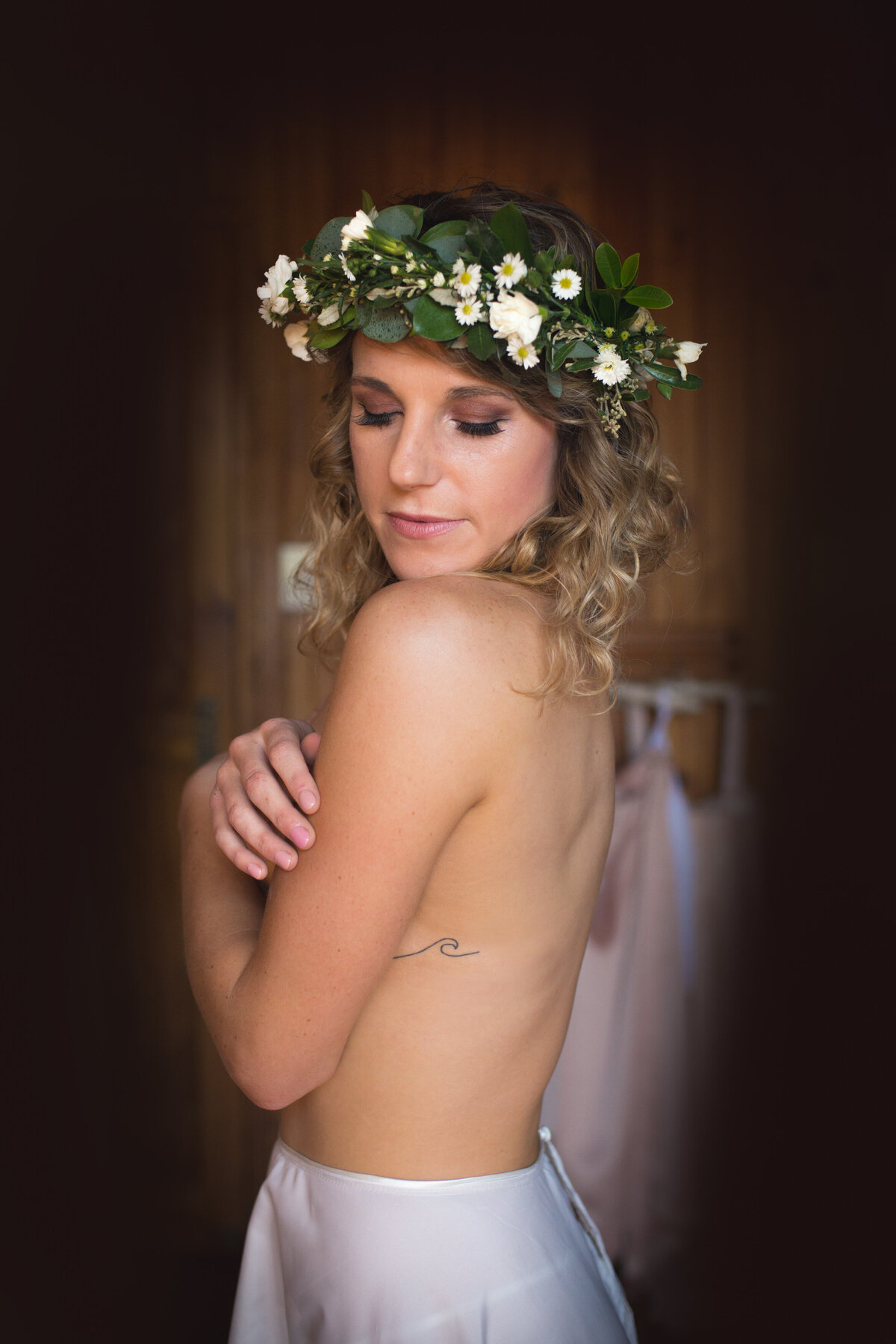 Topless bride crosses her arms and covers her breasts. Wearing a floral crown. 