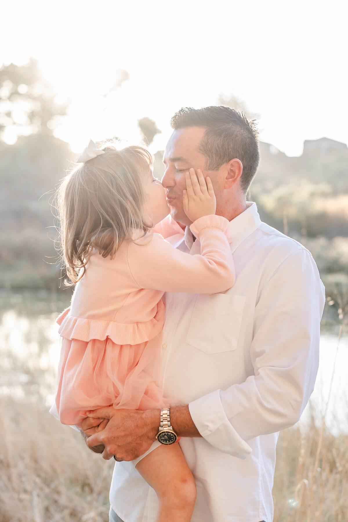 little girl in a pink dress holding her dad's face and kissing him