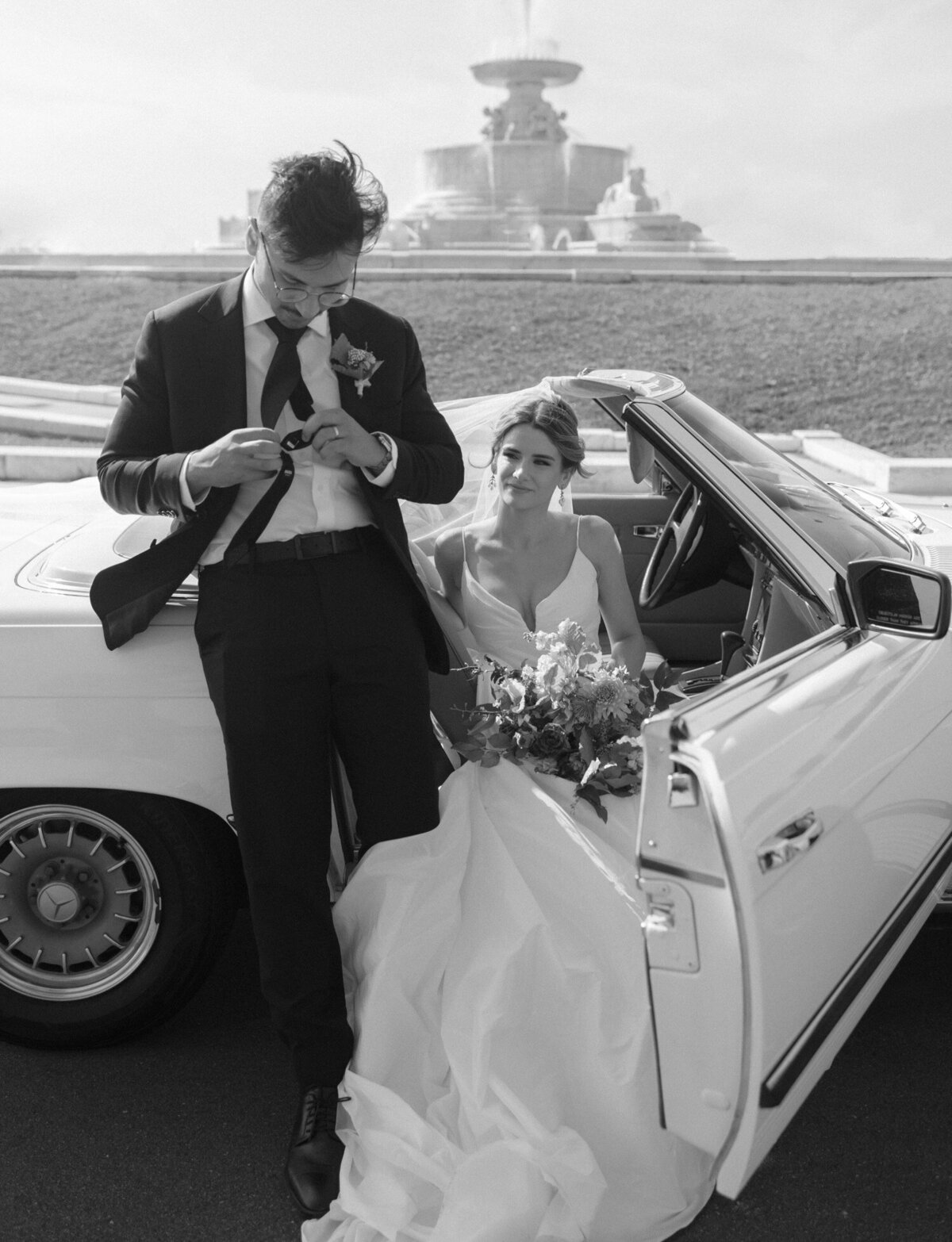 A bride & groom share a natural, relaxed moment with their vintage mercedes convertible wedding car in Detroit