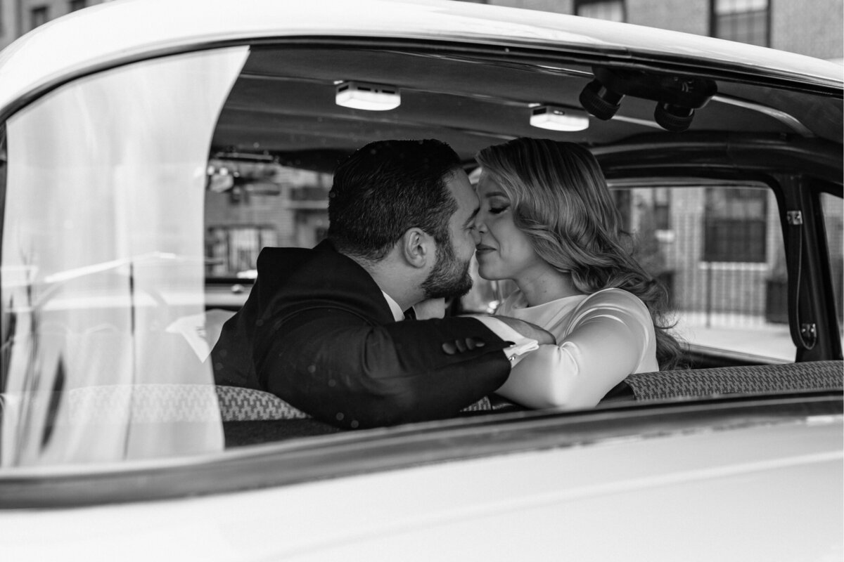 Bride and Groom sharing a kiss inside of a Taxi in a black and white photo.
