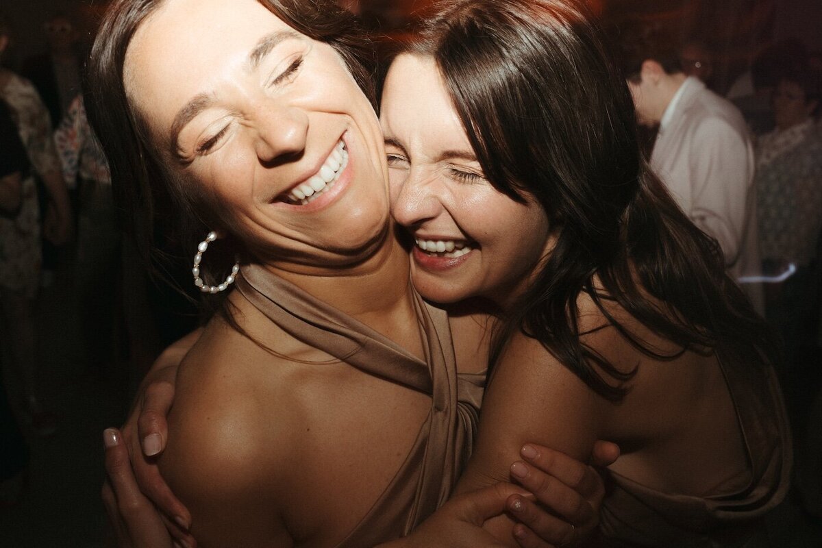 Deux femmes se serrent dans les bras, sourires complices et émotion palpable. Par Kamescop.