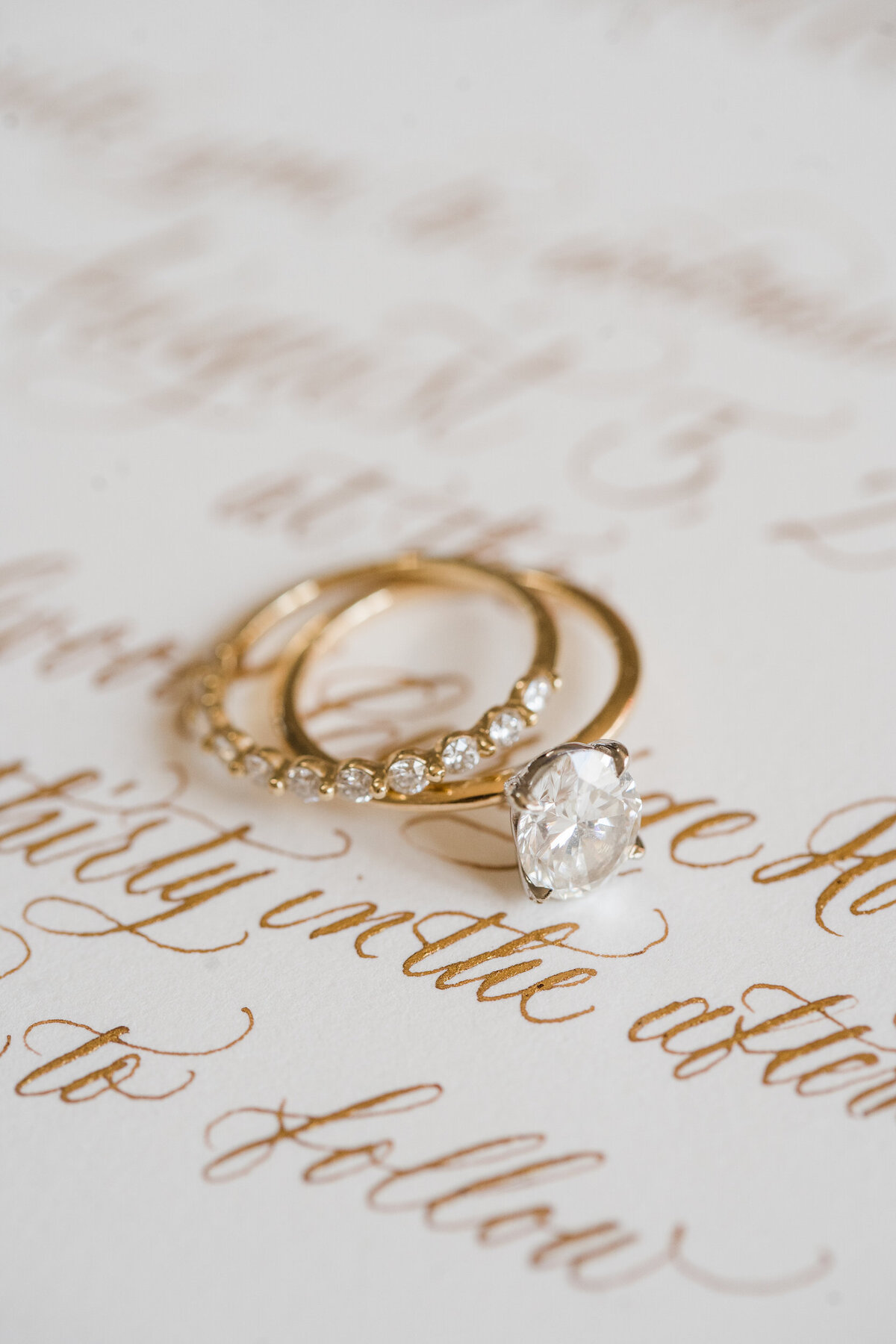 A gold wedding band and engagement ring sitting on gold calligraphy invitation for a Greensboro , NC wedding.