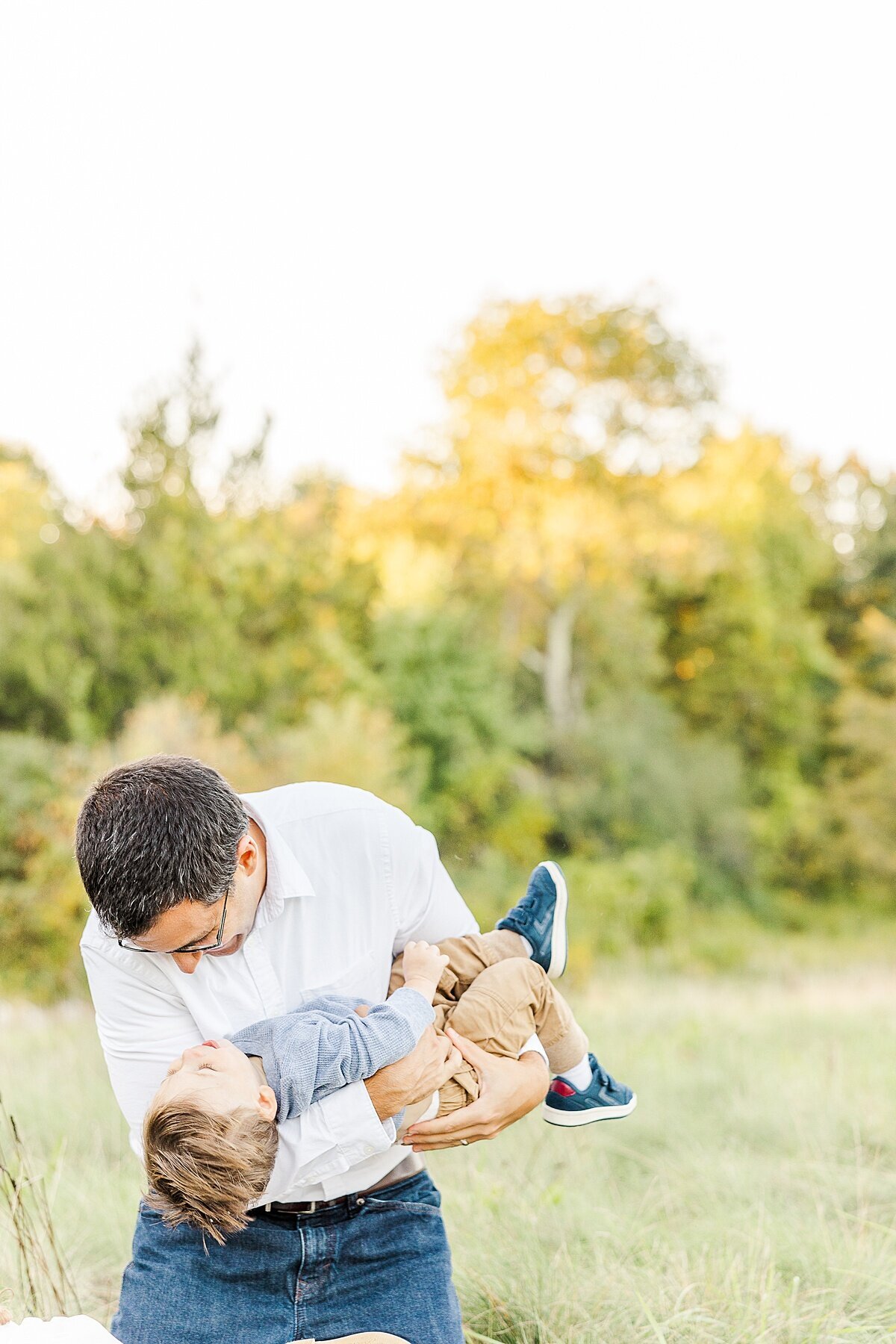 Dad hold son upside down during Family photo session with Sara Sniderman Photography a Oak Grove Park in Millis Massachusetts