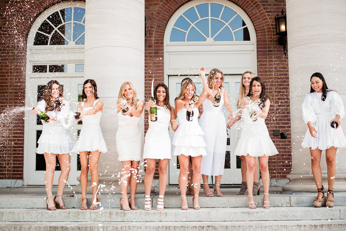 Vanderbilt college seniors popping champagne in white dresses on the steps at the University