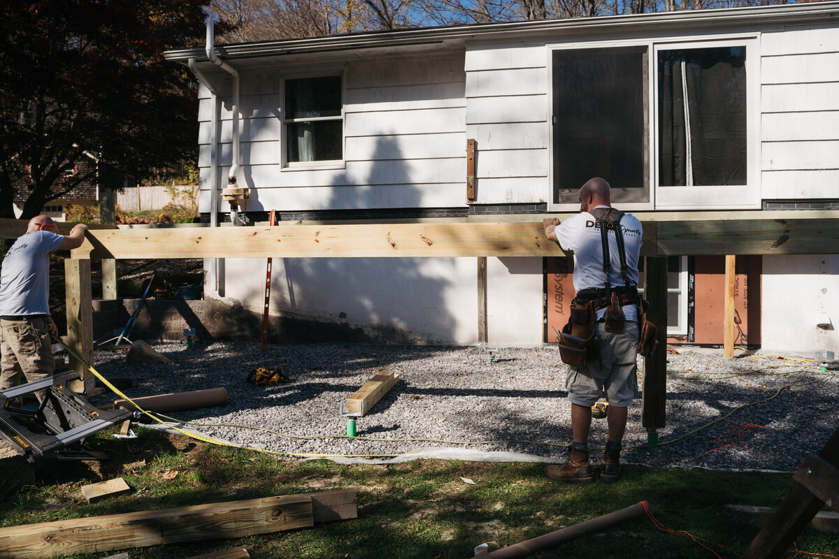 A team of Worcester Deck Builders mounting frame of a new deck on a white house