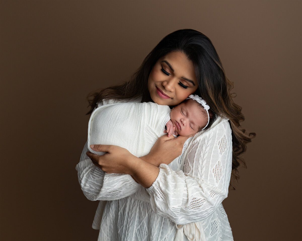 Studio portrait of a mother gently cradling her newborn baby, wrapped in soft white and captured in Paris, Ontario. A heartfelt addition to the Family Portfolio at Meraki Photographic Creations.