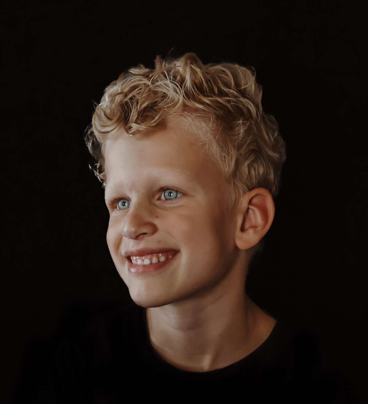 Een portret van een vrolijke jongen van de zijkant gefotografeerd tegen een donkere achtergrond