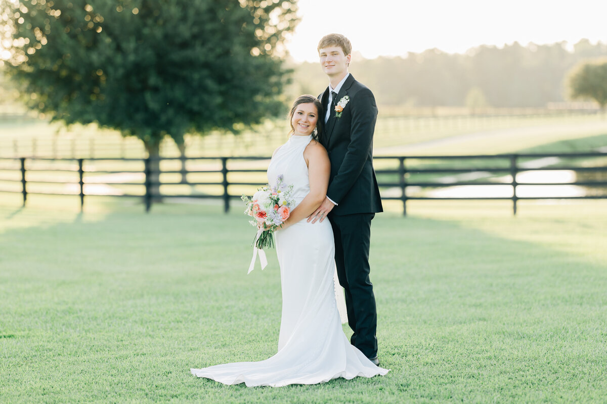 bride and groom embracing while standing in a farm field at sunset