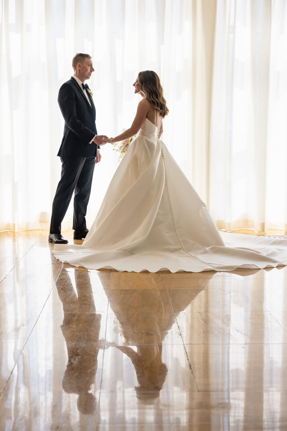 A bride and groom holding hands in front of a window
