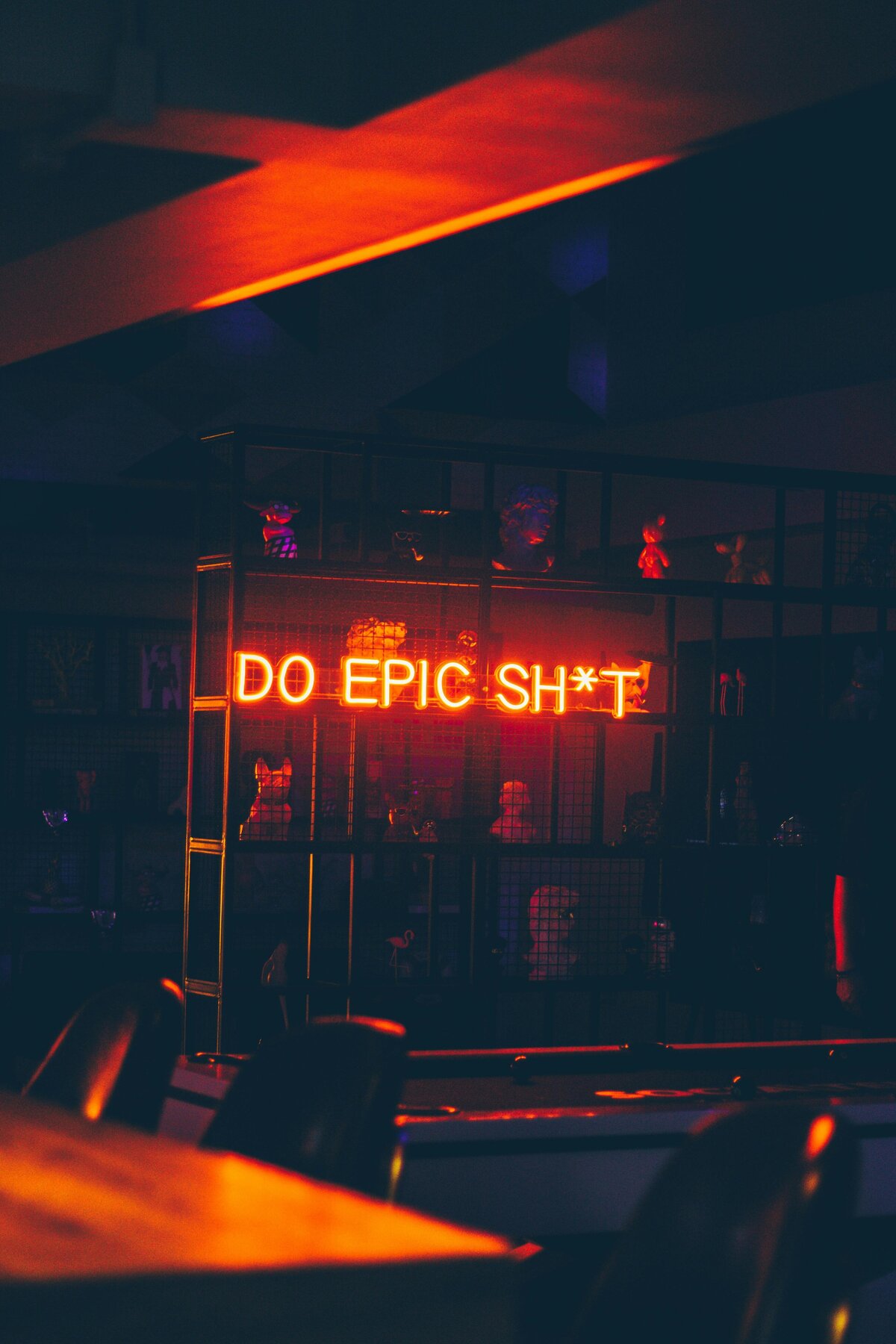Close-up of a neon sign in a dark setting that reads 'DO EPIC SHIT'.