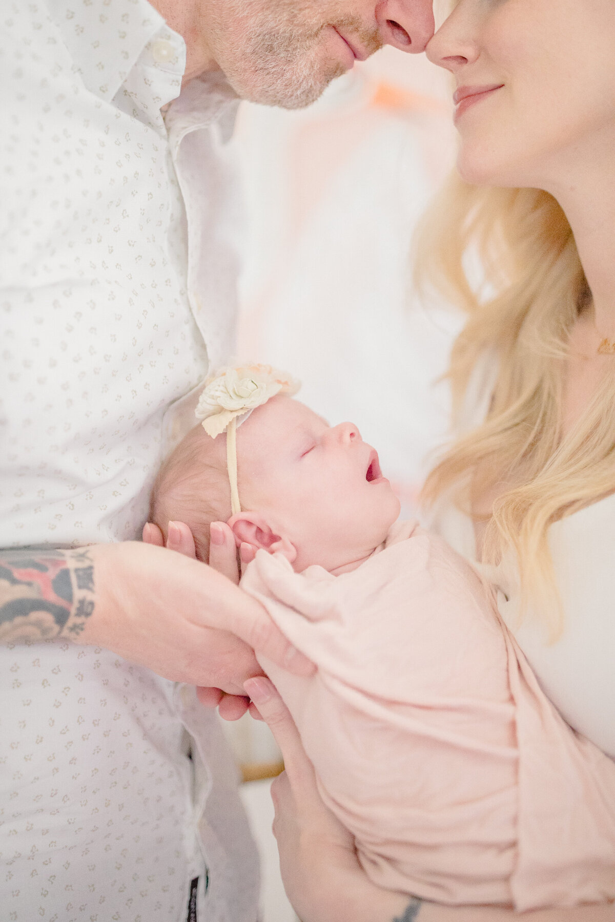 Close-up photo of a mother holding up her sleeping newborn, with only her hair visible as the focus remains on the baby. The image captures the newborn’s delicate features and peaceful expression in a soft, intimate moment
