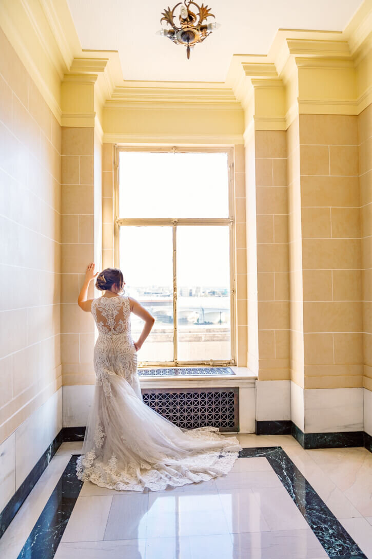 Bride looking out at the city of Dayton, OH after getting her dress on in the hallway with her mother,
