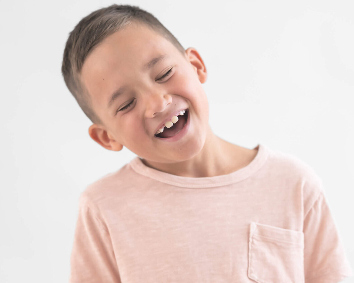 studio portrait of boy in pale pink shirt laughing and being silly