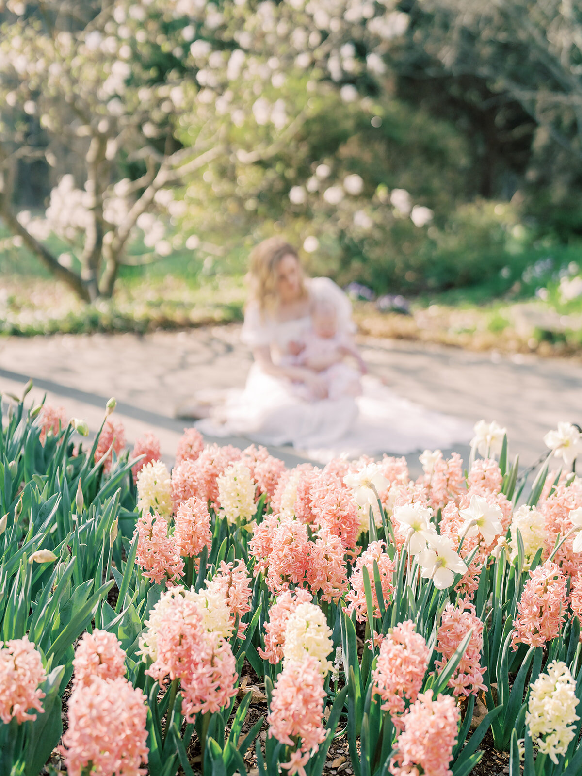 A mother sits with her baby girl in the background with pink hyacinths in the foreground.