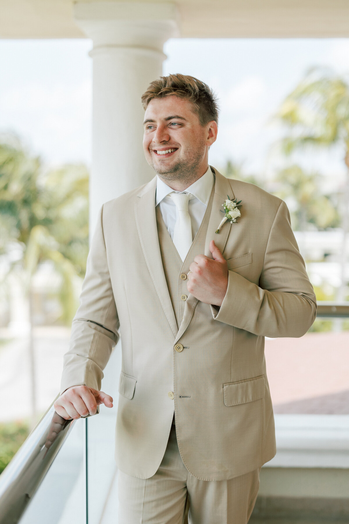 Groom on Cancun balcony adjusting boutonnière before wedding, captured by Philadelphia wedding photographer.