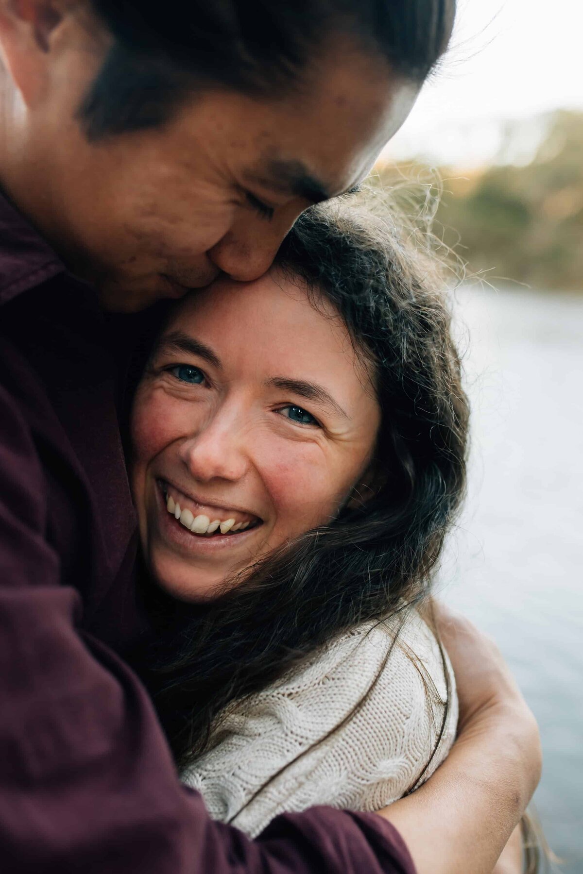 Proposal photography session with woman looking at camera, wrapped in fiancé's arms, Couples photoshoot, And So I Don't Forget Photography