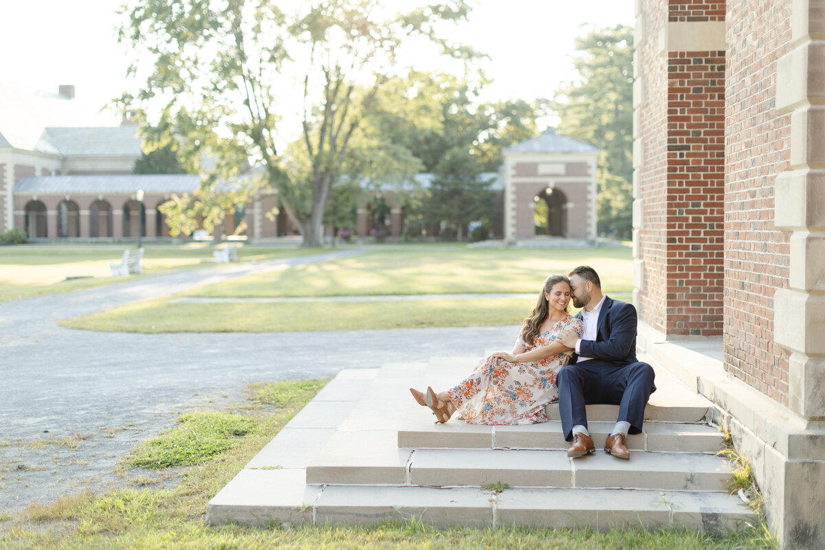 Engaged couple sit on the steps, snuggled close to each other