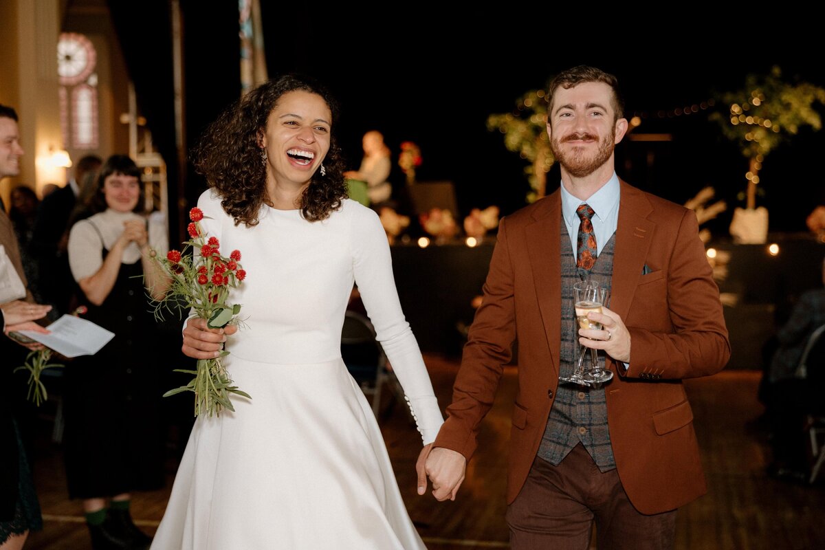 Bride and groom smiling happily at the guests as they walk hand in hand after the wedding