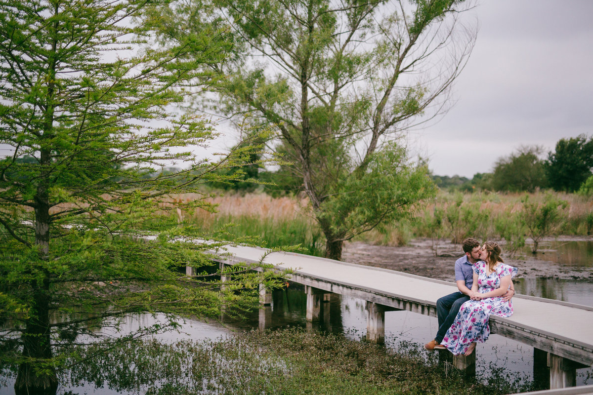 Couple sitting on the edge of a pier on a lake kissing at their engagement session.