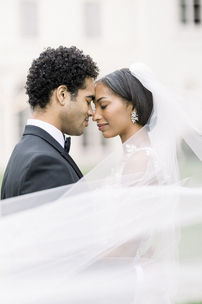 a bride and groom touching foreheads while wrapped in a veil
