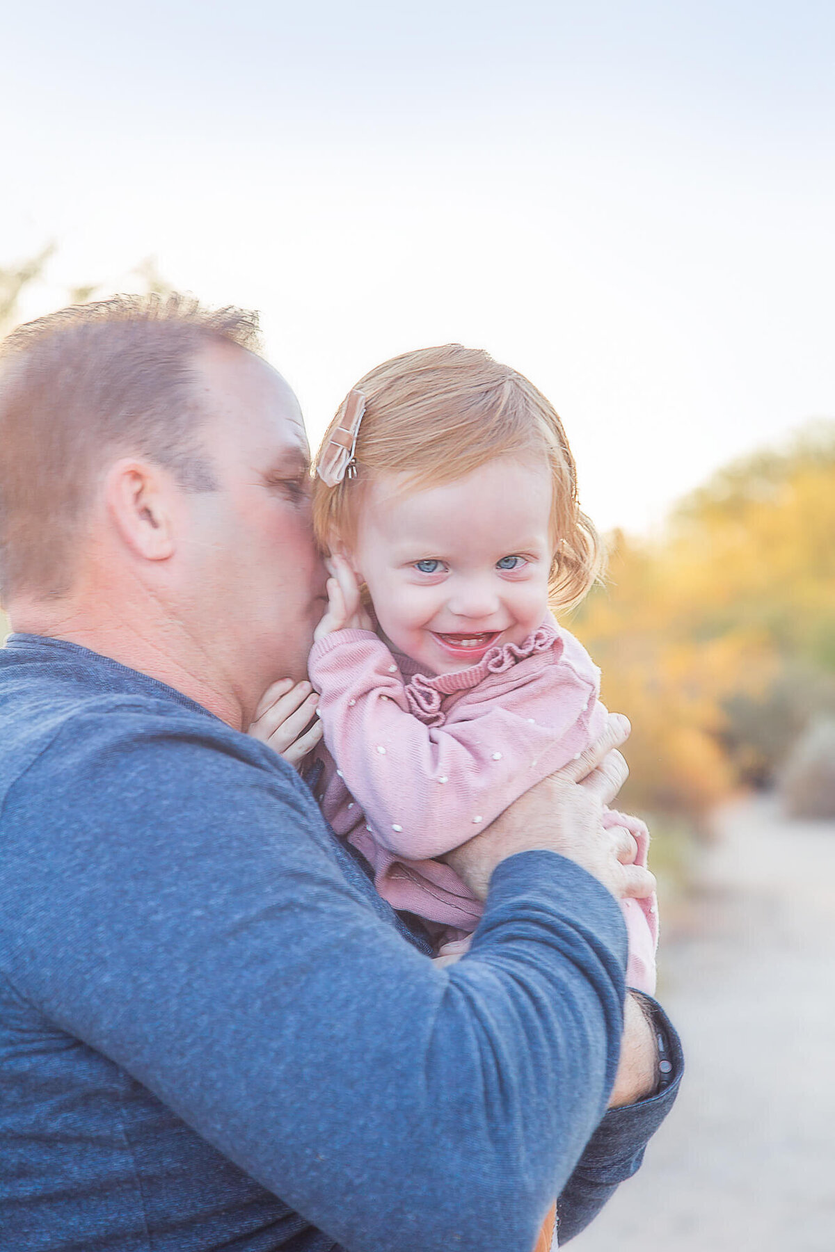 Happy toddler with red hair and blue eyes laughing from grandpa's kisses