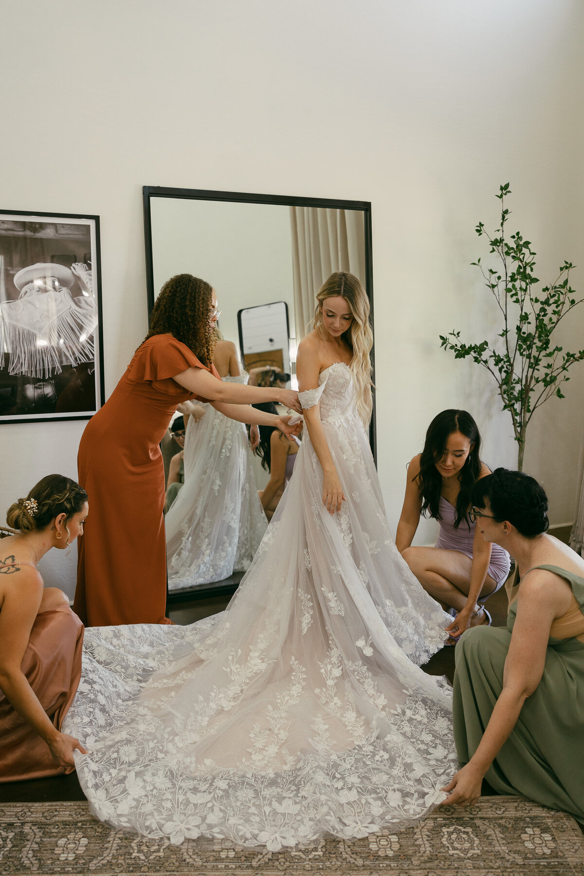 a bride gets ready in her dressing room with the help of her bridesmaids gathered around her