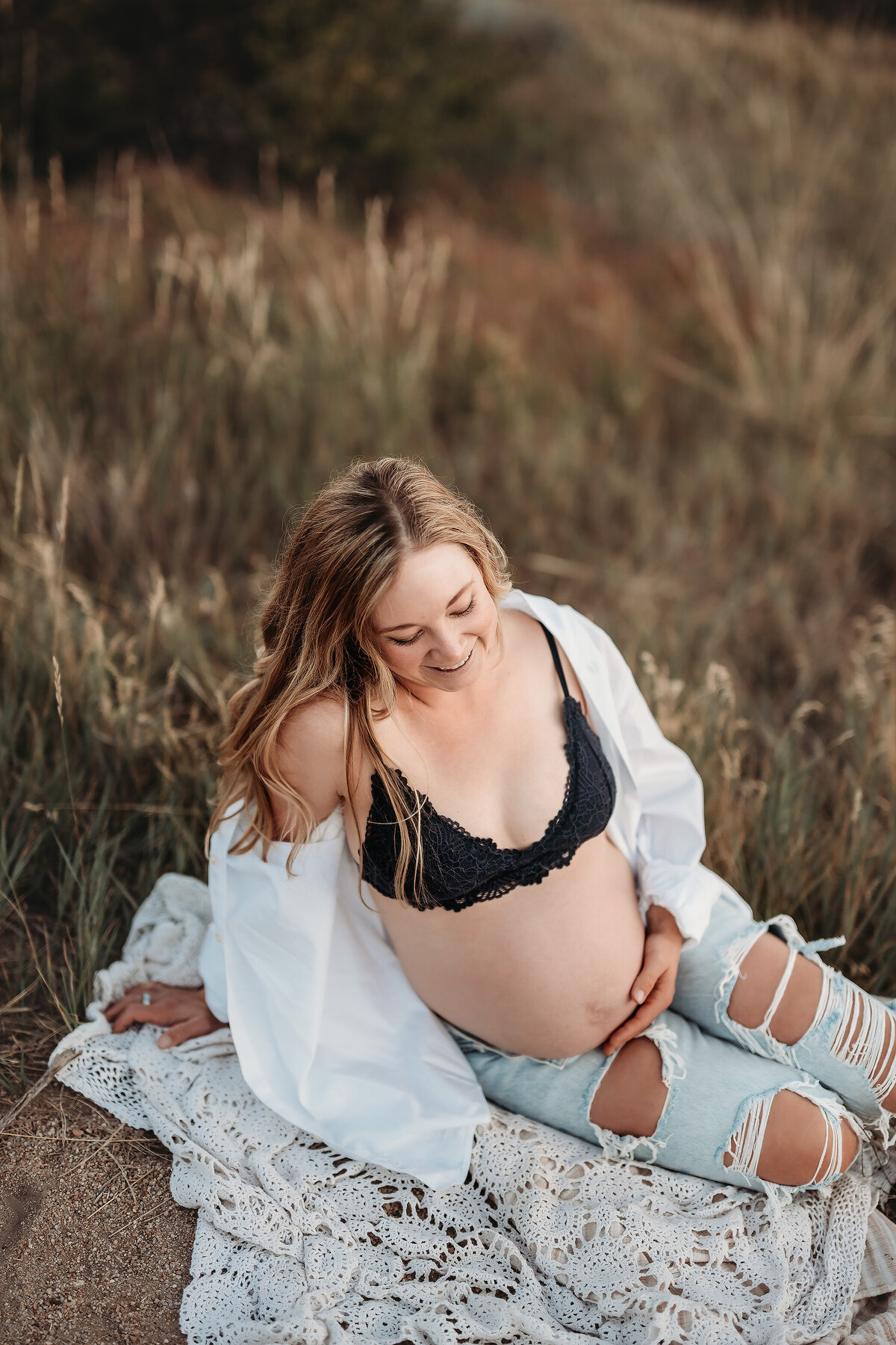 pregnant mother sitting on a blanket in a bra and jeans holding her belly