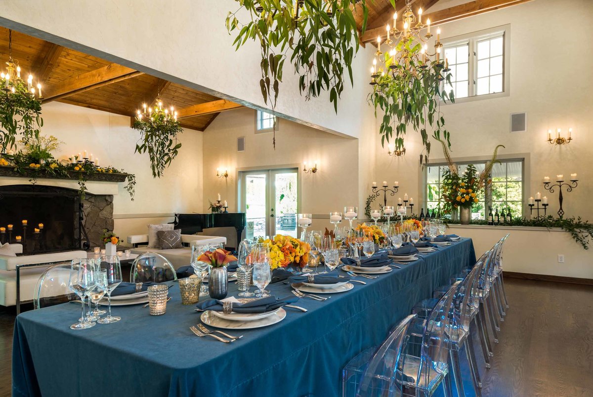 Chateau Lill company dinner party blue linens, clear ghost lucite chairs, greenery chandelier and orange flowers