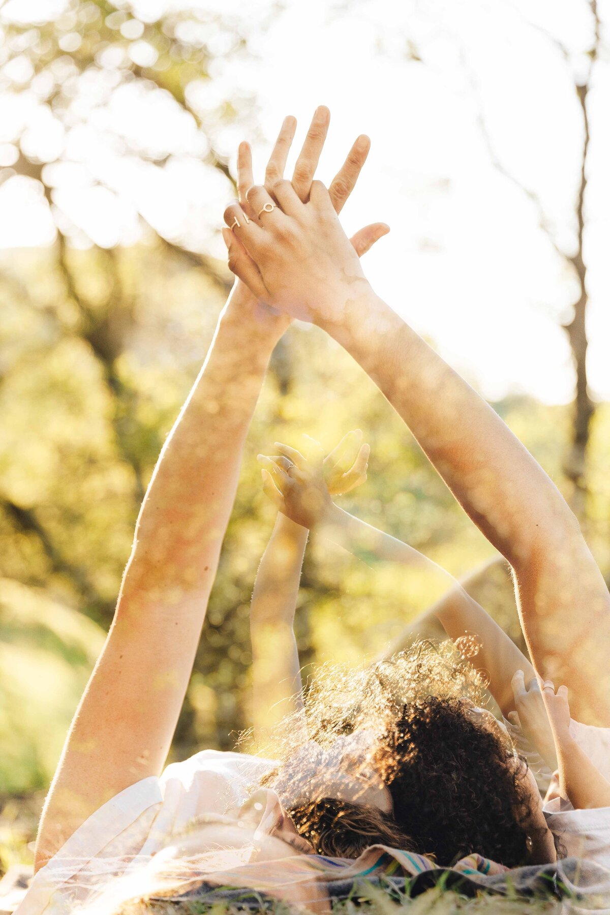 Mother and daughter are intertwining fingers as they  lay down in grass.