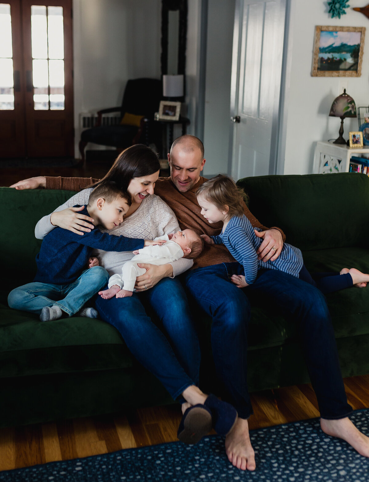 Mom and dad holding baby sitting on couch next to two young kids.