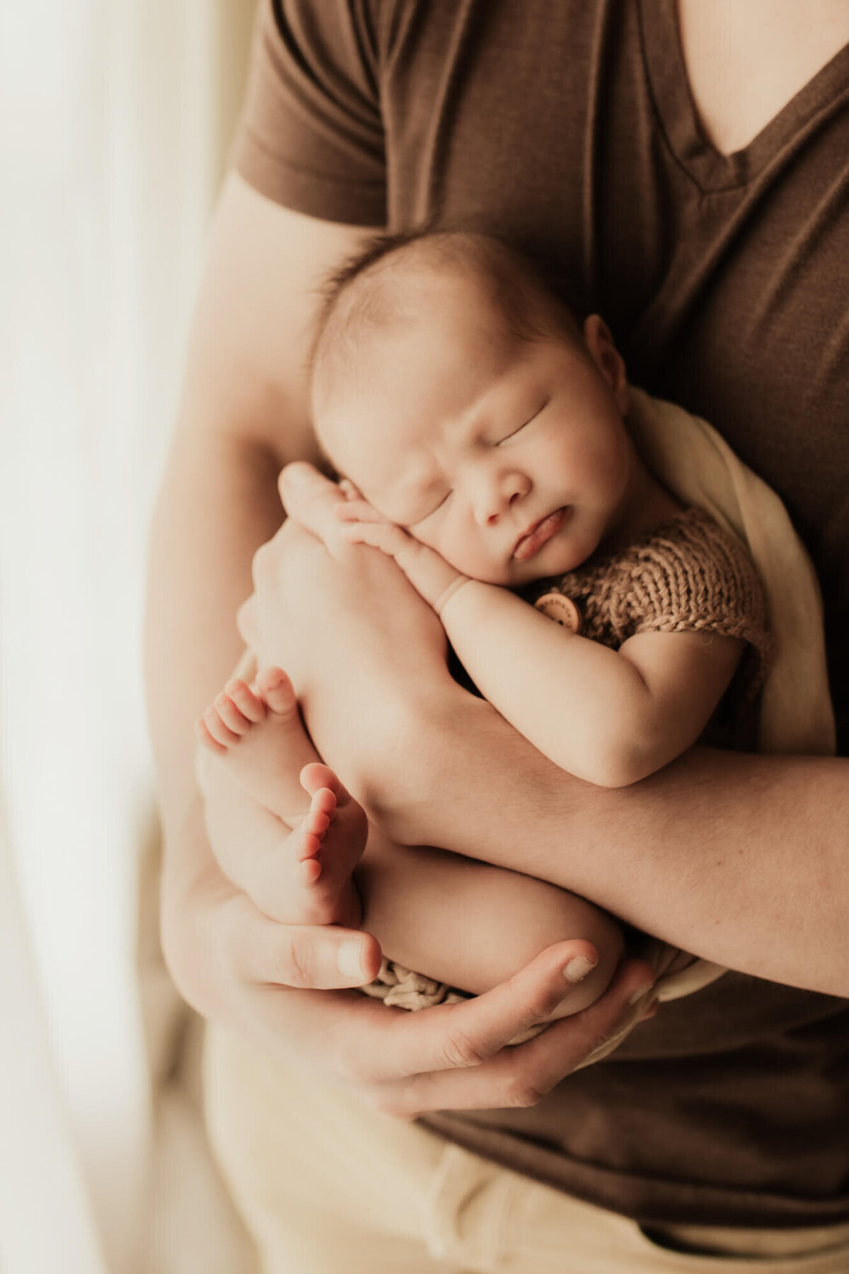Father holds his sleeping baby boy near a window for a studio photo in OKC.
