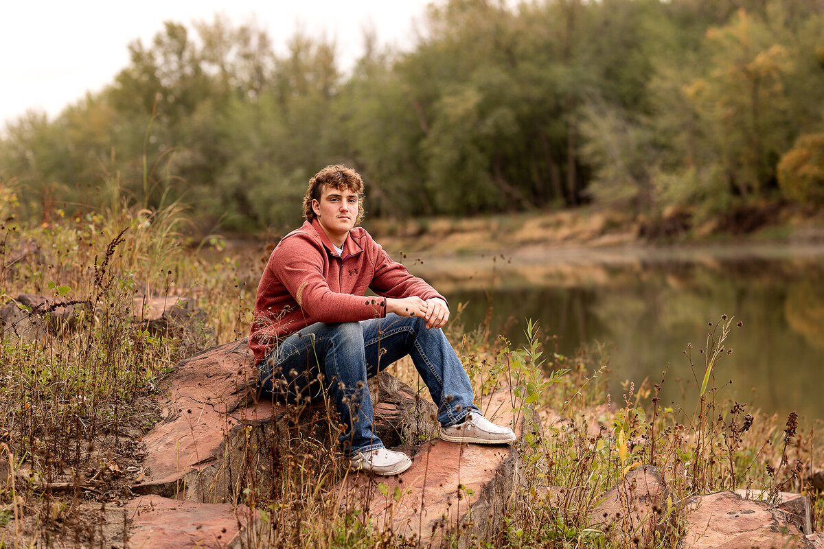 Senior guy sitting on a rock by the river.