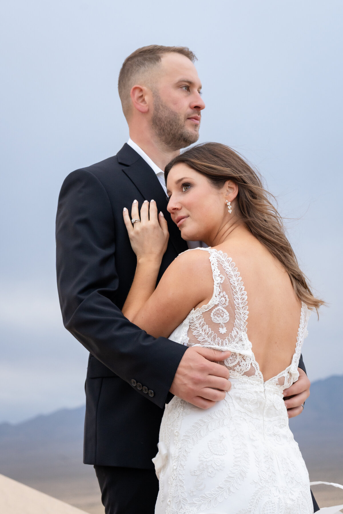 Bride and groom at Kelso Dunes during sunrise embracing while the bride, wearing Claire Pettibone, leans against his chest 