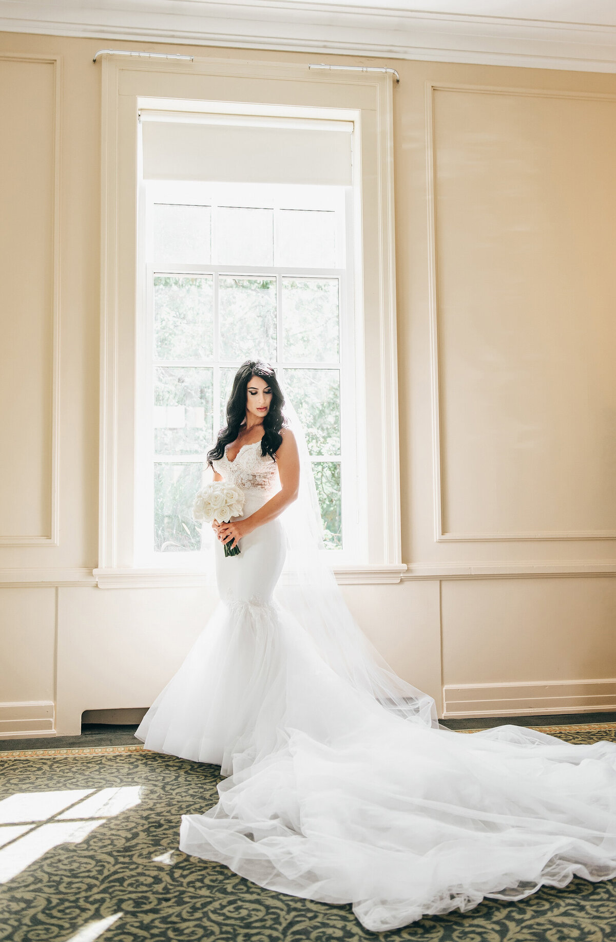 Glamorous bride posing in front of a window on her wedding days