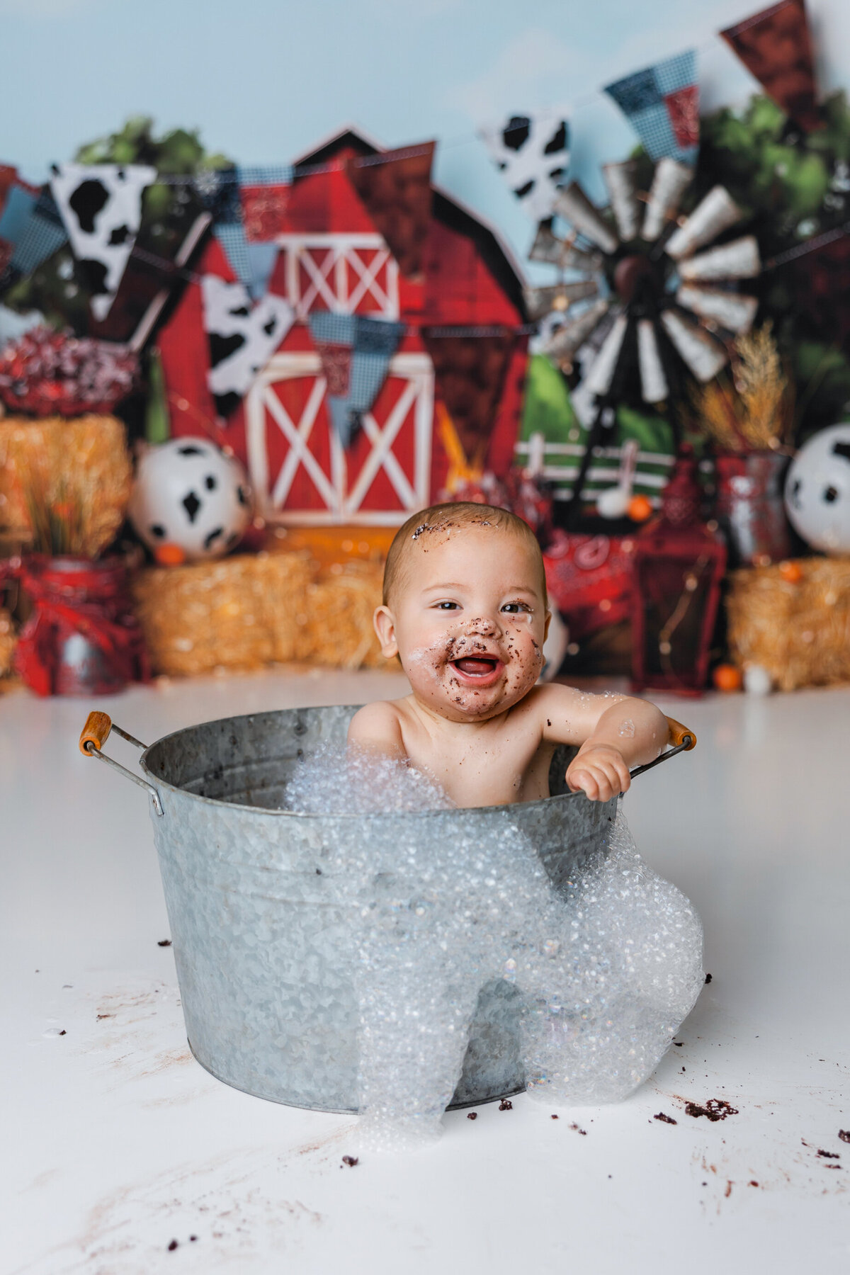 Baby with chocolate-covered face smiling in bubble bath after cake smash. Photograph by Yucaipa cake smash photographer Kaitlyn Dawn Photography.