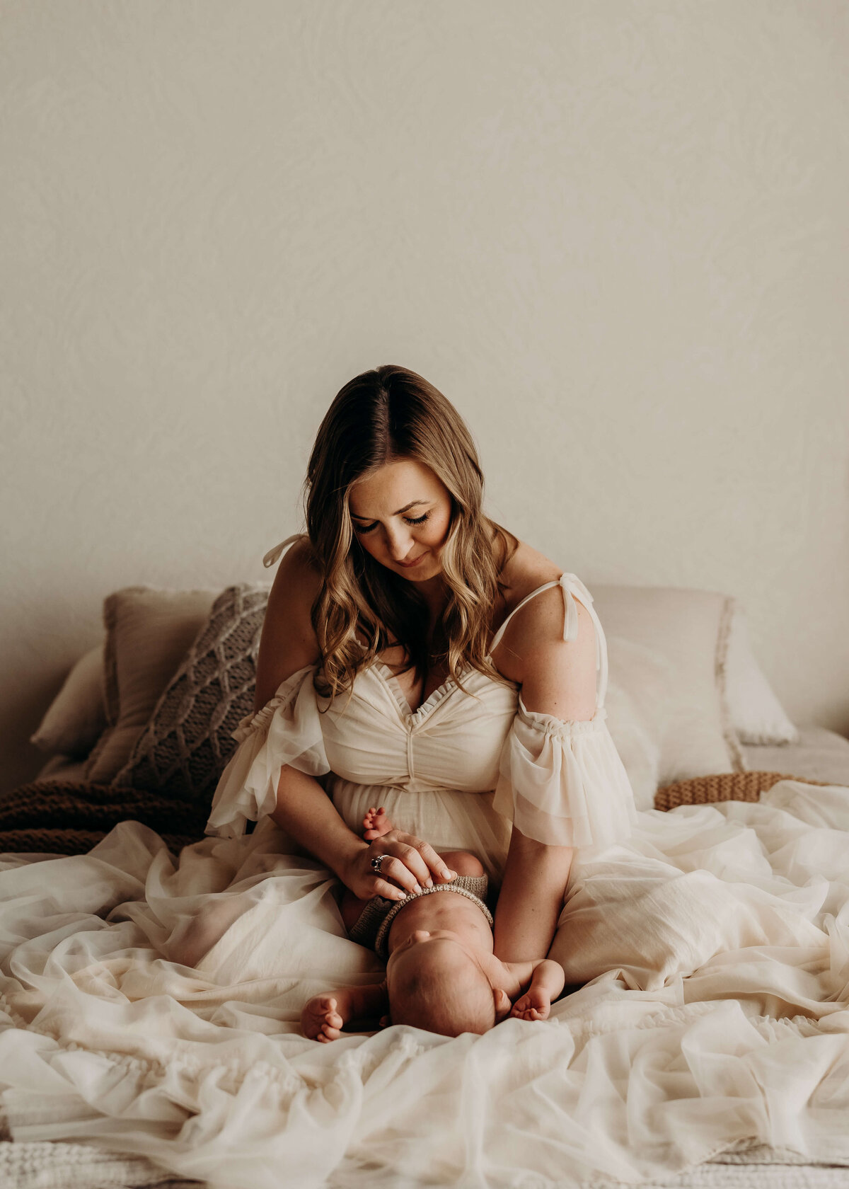 mother of a newborn holds her baby on a bed while wearing a chiffon gown
