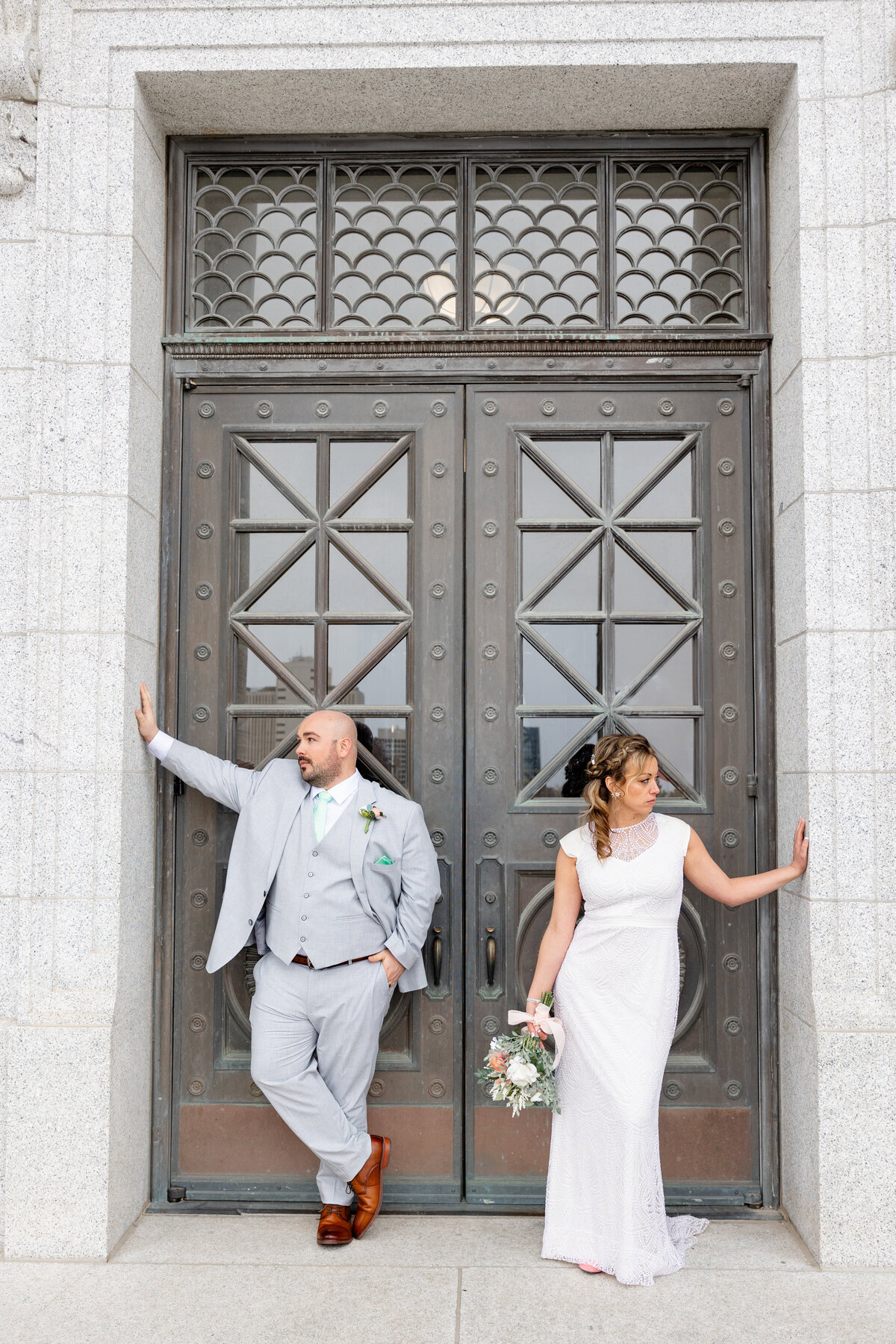 A bride and groom pose stylishly against the intricate iron doors of the Utah State Capitol, striking a confident and modern look.