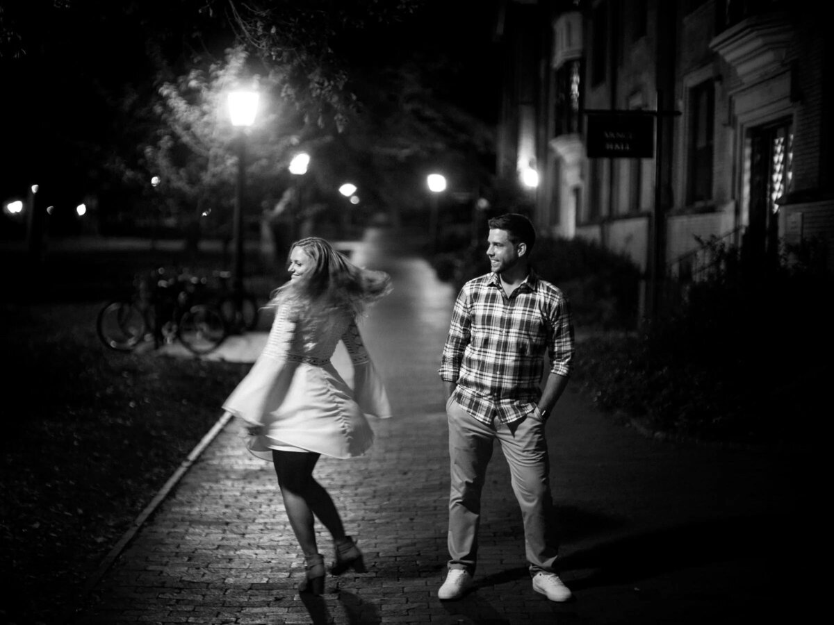 Black and white night-time image of a couple walking down a brick-lined street