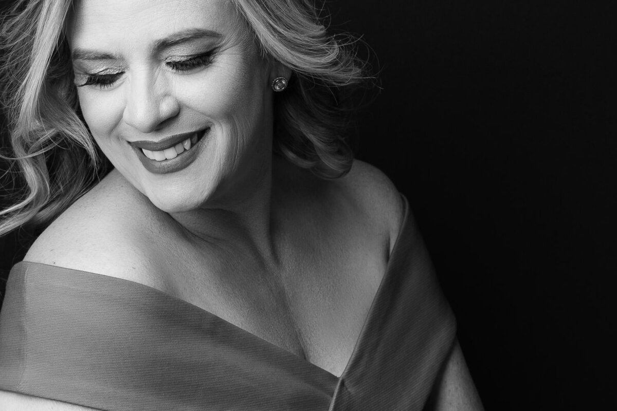 Studio portrait of an older woman in a low-cut gown, smiling warmly as she gazes off-camera, exuding grace and charm.