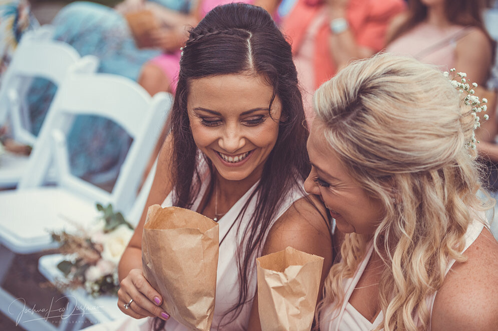 Two ladies giggling to each other holding brown bags of confetti