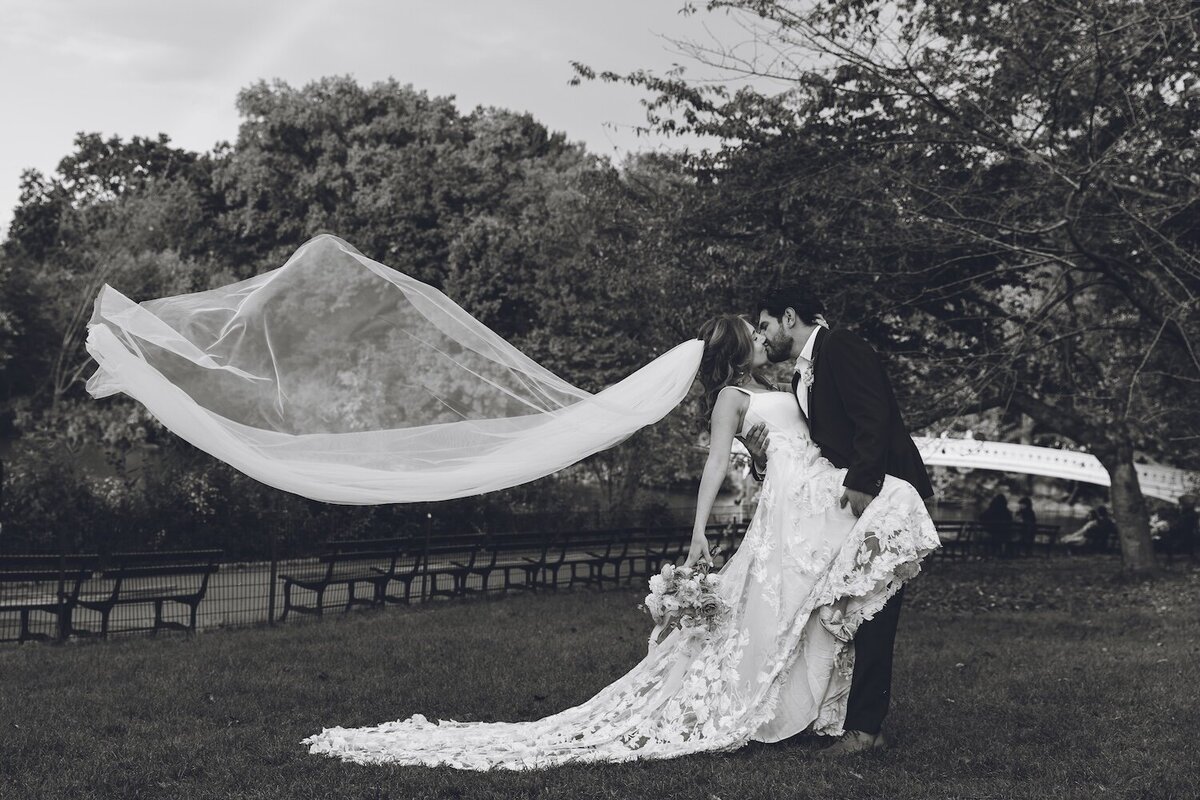 Bride and groom posing with floating veil in black and white