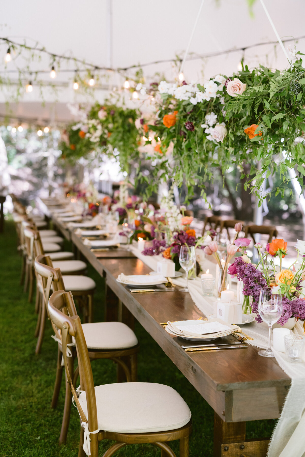 Wood harvest table with overhead floral installation under a tent at a cottage wedding in Ontario