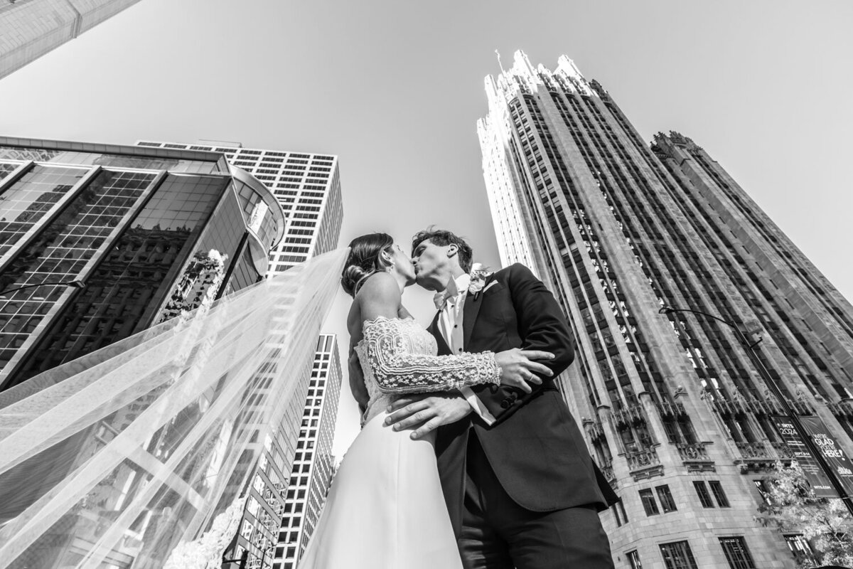 A bride and groom kissing in front of a tall building