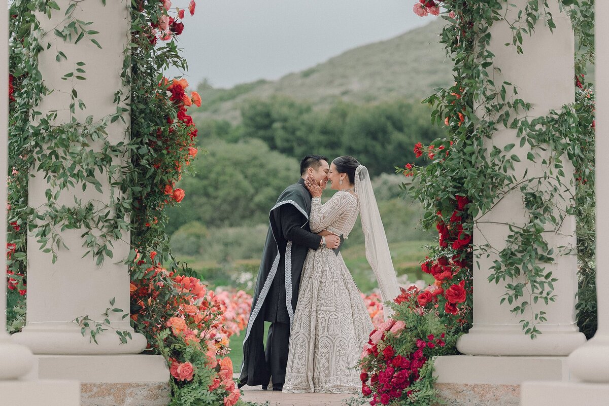Wedding couple kissing under flower dripped pillars at The Resort at Pelican Hill