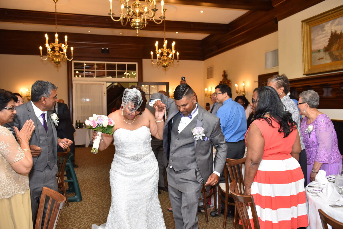 Newlyweds entering wedding reception, guests applauding.